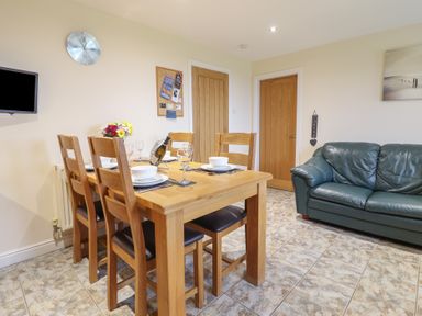 A dining area with a wooden table and chairs set with dishes next to a green leather sofa at Ysgubor Newydd Parc Isaf in Dyffryn Ardudwy
