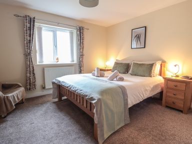 A bedroom with a double bed and rolled towels on it with nightstands and lamps at Ysgubor Newydd Parc Isaf in Dyffryn Ardudwy