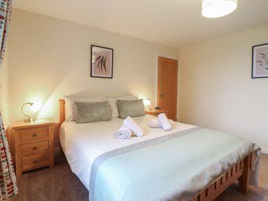 A bedroom with a double bed two bedside tables with lamps and rolled towels on the bed at Ysgubor Newydd Parc Isaf Dyffryn Ardudwy