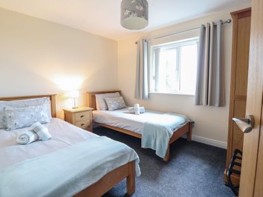 A bedroom with two single beds separated by a wooden nightstand with a lamp at Ysgubor Newydd Parc Isaf in Dyffryn Ardudwy