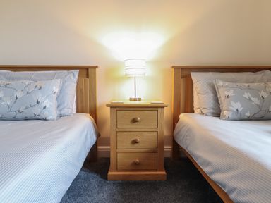 A bedroom with two single beds separated by a wooden nightstand with a lamp on top at Ysgubor Newydd Parc Isaf in Dyffryn Ardudwy