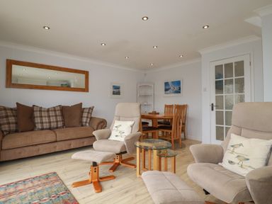 A living room with beige armchairs a brown sofa dining table and chairs and a glass side table at 3 The Bowling Green in St Just in Roseland near St Mawes