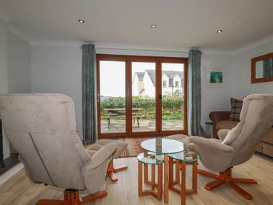 A living room with two armchairs a glass coffee table next to a sliding door at 3 The Bowling Green in St Just in Roseland near St Mawes