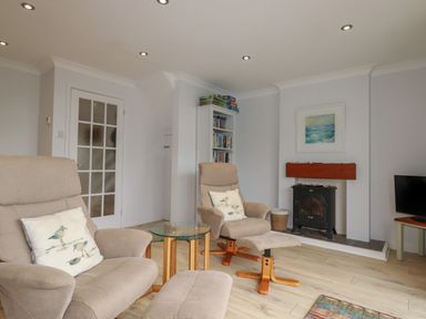 A sitting room with two armchairs a glass side table a bookshelf a wood stove and a television at 3 The Bowling Green in St Just in Roseland near St Mawes