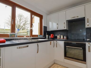 A kitchen with white cabinets black countertops a window and an oven at 3 The Bowling Green in St Just in Roseland near St Mawes