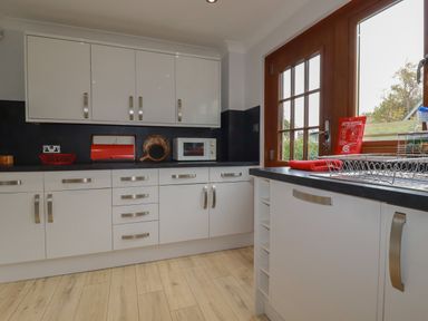 A kitchen with white cabinets black countertops a microwave a bread bin and a wooden door with glass panels at 3 The Bowling Green in St Just in Roseland near St Mawes