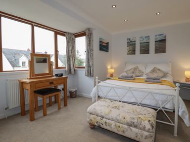 A bedroom with a bed bedside tables lamps dressing table window and floral bench at 3 The Bowling Green in St Just in Roseland near St Mawes