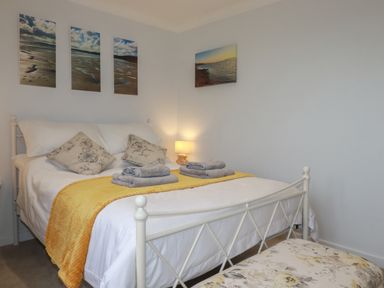 A bedroom with a white metal bed frame with cushions and folded towels on the bed at 3 The Bowling Green in St Just in Roseland near St Mawes