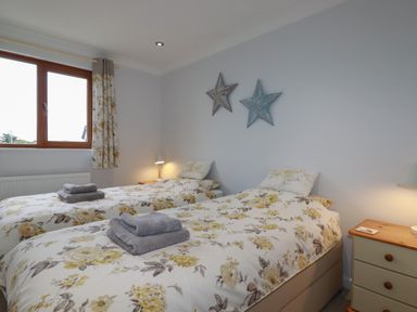 A bedroom with two single beds with floral bedding and folded towels by a window at 3 The Bowling Green in St Just in Roseland near St Mawes