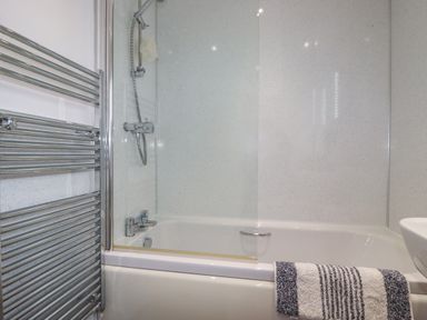 A bathroom with a bathtub shower combination a glass shower screen a chrome towel radiator and a towel on the tub at 3 The Bowling Green in St Just in Roseland near St Mawes