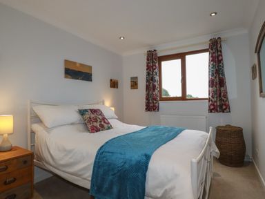 A bedroom with a double bed a bedside table with a lamp a window with floral curtains and a wicker basket at 3 The Bowling Green in St Just in Roseland near St Mawes
