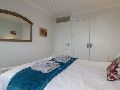 A bedroom with a bed with folded towels and a blue runner a mirror a door and a closet at 3 The Bowling Green in St Just in Roseland near St Mawes