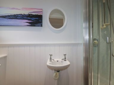A bathroom with a small sink with two taps a round mirror a shower enclosure and a wall painting at 3 The Bowling Green in St Just in Roseland near St Mawes