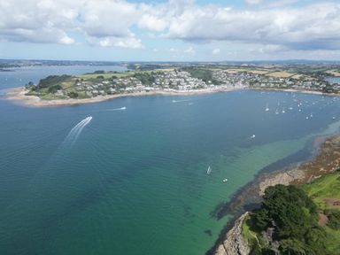 A coastal view of a village with boats in the water and green fields at 3 The Bowling Green in St Just in Roseland near St Mawes