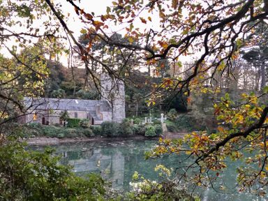 A stone church beside a body of water surrounded by trees with autumn leaves at 3 The Bowling Green in St Just in Roseland near St Mawes