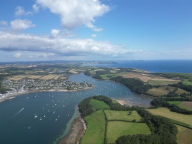An aerial view of a river estuary with boats moored near a town and surrounding fields at 3 The Bowling Green in St Just in Roseland near St Mawes