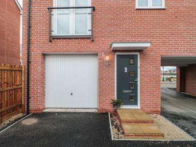A front entrance with a dark door numbered 3 and a white garage door on a red brick house with a small porch and driveway at Cotswold Outlet Coach House in Tewkesbury