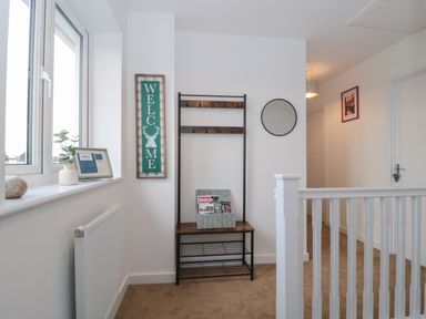 A hallway with a coat rack bench mirror and welcome sign at Cotswold Outlet Coach House in Tewkesbury