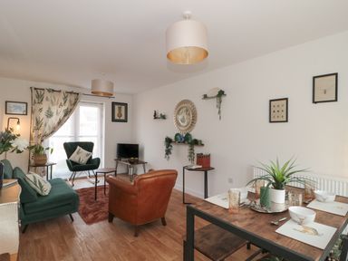 A living room with green and brown chairs a wooden dining table with place settings and plants at Cotswold Outlet Coach House in Tewkesbury