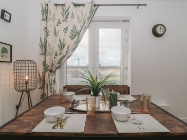 A dining table set with four animal-themed placemats bowls and glasses near a window with botanical curtains at Cotswold Outlet Coach House in Tewkesbury