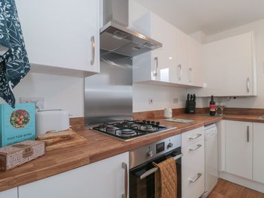 A kitchen with white cabinets wooden countertops a gas stove an oven a toaster bread knives a cookbook a bottle of wine and wine glasses at Cotswold Outlet Coach House in Tewkesbury