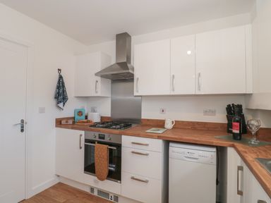 A kitchen with white cabinets wooden countertops a gas stove oven a dishwasher and kitchen utensils at Cotswold Outlet Coach House in Tewkesbury