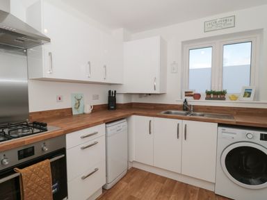 A kitchen with white cabinets wooden countertops a gas stove an oven a dishwasher a washing machine and a window with plants on the sill at Cotswold Outlet Coach House in Tewkesbury