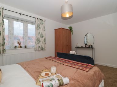 A bedroom with a bed a wardrobe a dressing table with a mirror and a window with patterned curtains at Cotswold Outlet Coach House in Tewkesbury