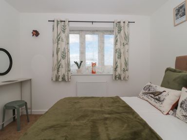 A bedroom with a bed with green bedding and animal print pillows by a window with curtains and a small desk with a stool at Cotswold Outlet Coach House Tewkesbury