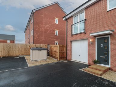 A driveway with a closed garage door and front door of a brick house with a fence and storage shed in the background at Cotswold Outlet Coach House in Tewkesbury