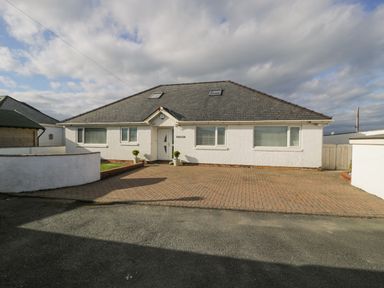 A white house with a grey tiled roof and paved driveway at The Gables in Tywyn