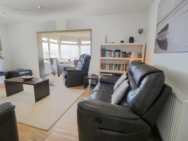 A living room with black leather sofas and a bookcase at The Gables in Tywyn