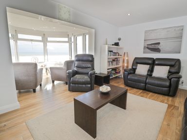 A living room with leather sofas a coffee table a bookshelf and large windows overlooking the sea at The Gables in Tywyn