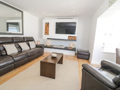 A living room with a leather sofa armchair coffee table and a wall mounted television at The Gables in Tywyn