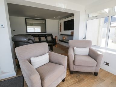 A living room with two beige armchairs and a black leather sofa with a wall-mounted TV at The Gables in Tywyn