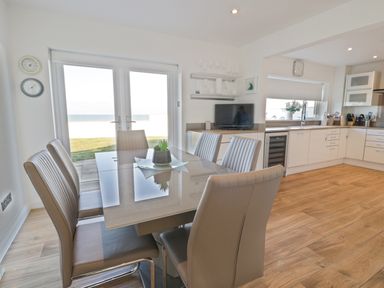 A dining area with a table and six chairs next to glass doors and a kitchen with white cabinets and wooden floor at The Gables in Tywyn
