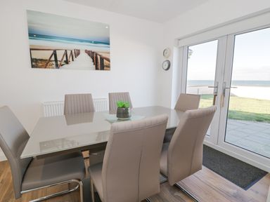 A dining room with a glass table six chairs and a large window showing a garden and sea view at The Gables in Tywyn