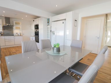 A kitchen and dining area with a glass table and six chairs a white double door fridge ovens and wooden floor at The Gables in Tywyn