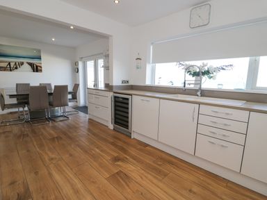 A kitchen with white cabinets a sink a wine cooler and a dining area with table and chairs at The Gables in Tywyn