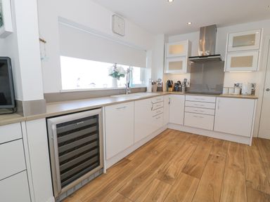 A modern kitchen with white cabinets wooden floor a wine cooler and a large window at The Gables in Tywyn