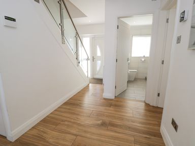 A hallway with wooden flooring a staircase with glass panels a white front door and an open door leading to a bathroom at The Gables in Tywyn