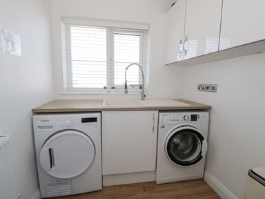 A laundry room with a washing machine a dryer a sink and wall cabinets at The Gables in Tywyn