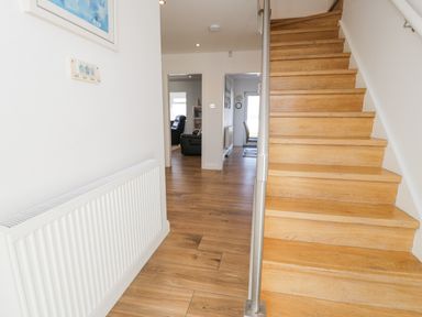 A hallway with wooden stairs and wooden floor leading to rooms with furniture at The Gables in Tywyn