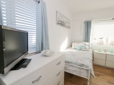 A bedroom with a single bed dresser and television by the window at The Gables in Tywyn