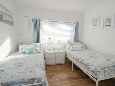 A bedroom with two single beds separated by a white nightstand with lamps and a clock at The Gables in Tywyn