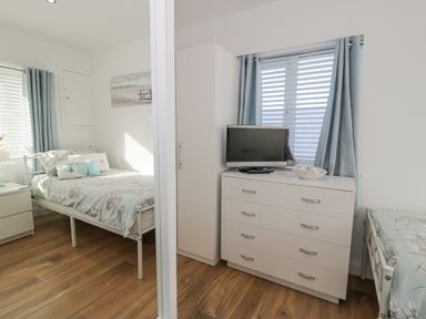 A bedroom with two single beds a white dresser with a TV on top and blue curtains at The Gables in Tywyn
