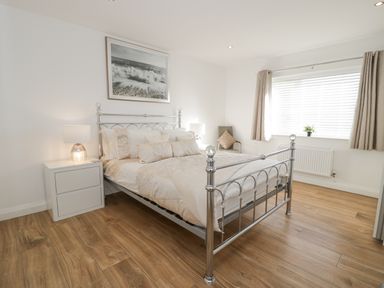 A bedroom with a metal bed frame two bedside tables lamps and a window with blinds and curtains at The Gables in Tywyn