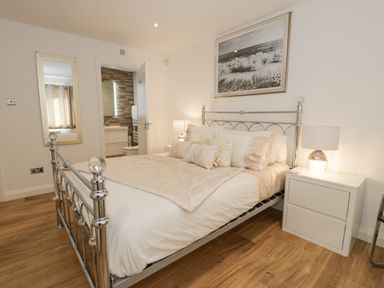 A bedroom with a metal bed frame bedside tables with lamps a wall mirror and an open door to a bathroom at The Gables in Tywyn