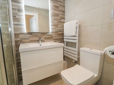 A bathroom with a vanity sink a lit mirror a towel rack with a white towel and a toilet at The Gables in Tywyn