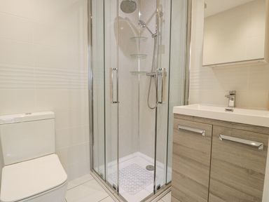 A bathroom with a toilet a glass shower enclosure and a sink with wooden cabinet at The Gables in Tywyn